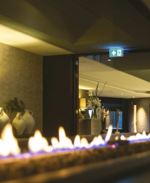 Atmosférické hotelové prostředí s liniovým plynovým krbem a decentním únikovým osvětlením.