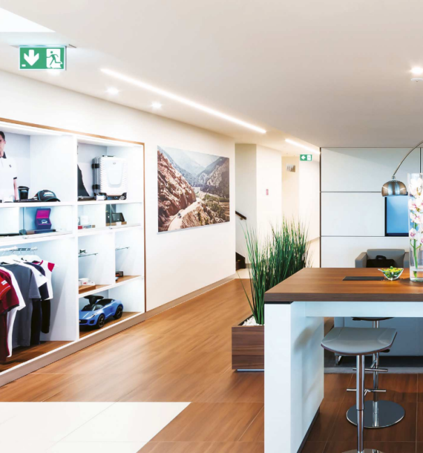 Designový showroom s výstavními policemi, barovým pultem a lineárním LED osvětlením podél stropu.