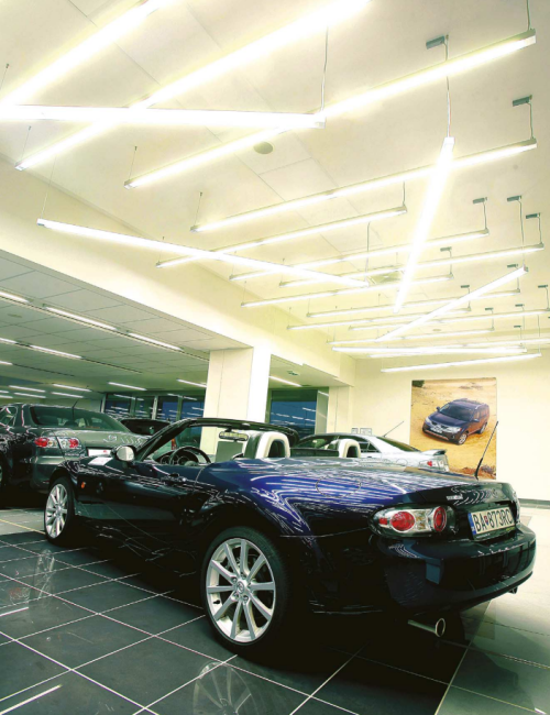 Autosalon s vystavenými vozidly a netradičně uspořádaným závěsným LED osvětlením na stropě.