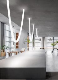 Závěsné LED svítidlo v dynamických, zakřivených liniích na tmavém stropě.